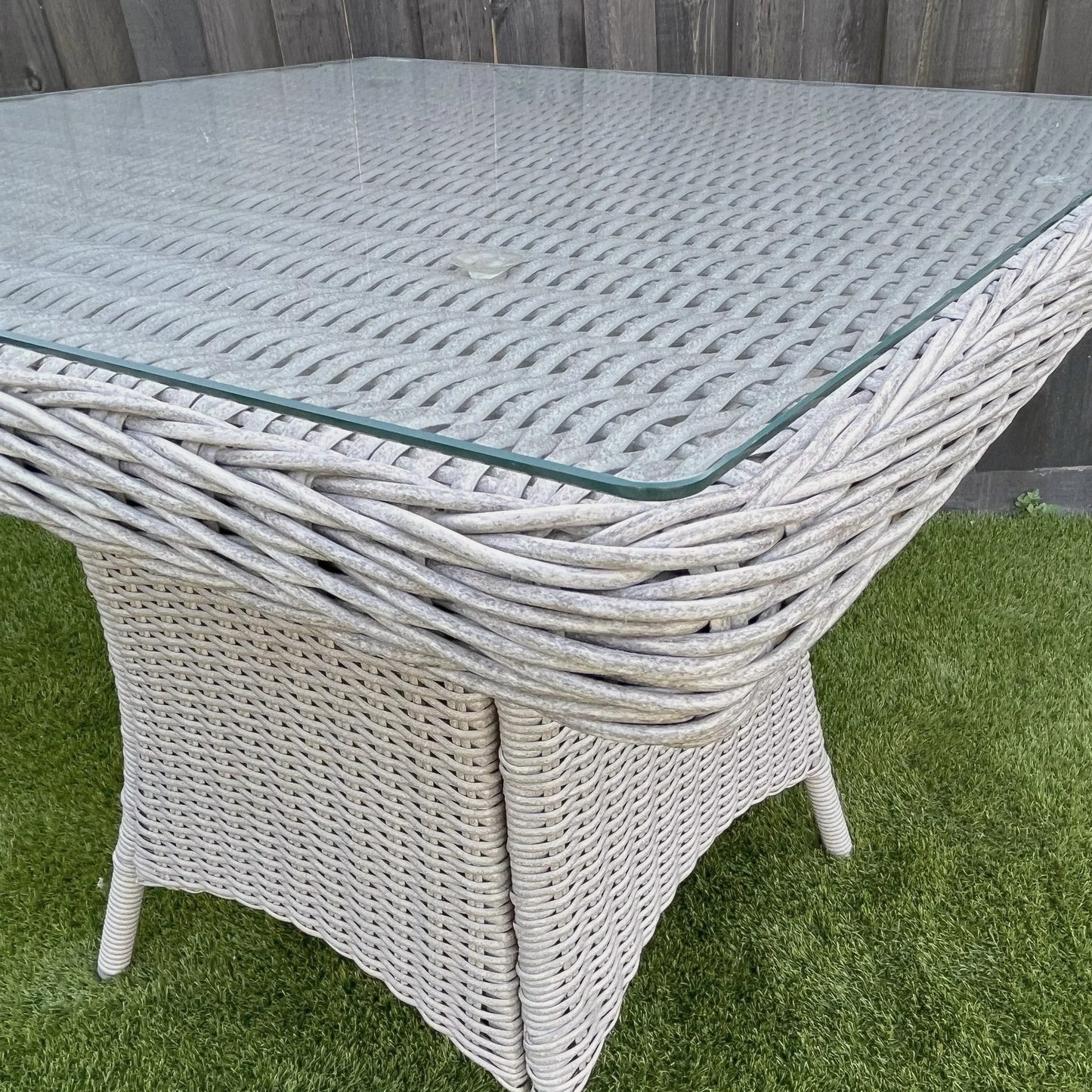 Grey square outdoor wicker dining table with glass top on green artificial grass
