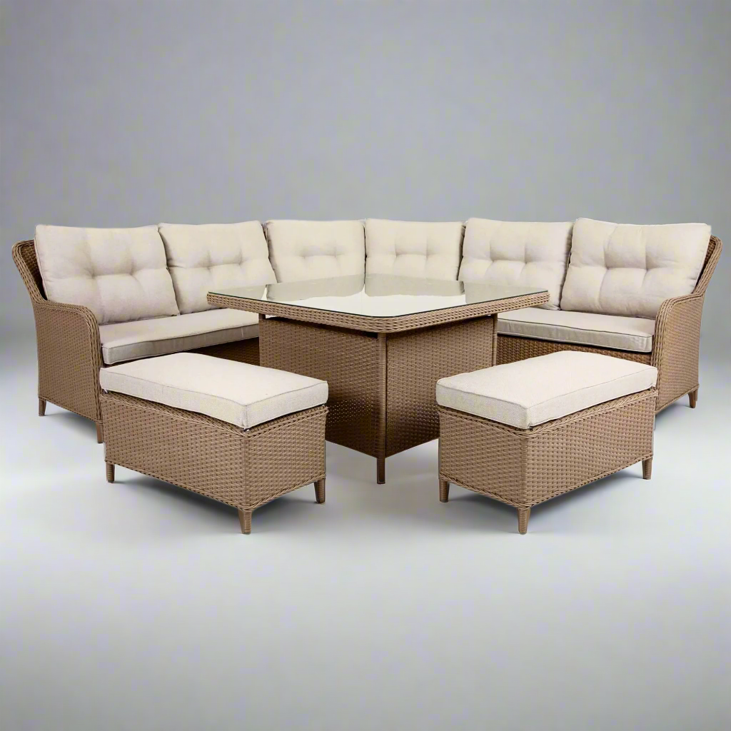 An outdoor lounge set made of poly rattan wicker in natural brown color, with beige cushions, including a corner sofa, two ottomans, and a dining table.