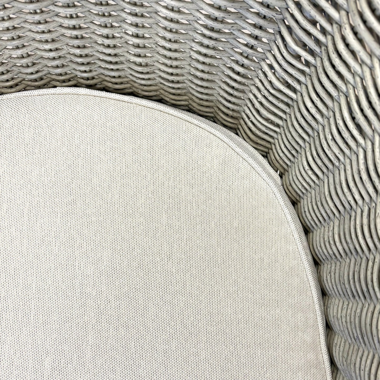 Close-up of grey woven rattan wicker chair with beige cushion, showcasing texture and craftsmanship for outdoor furniture.