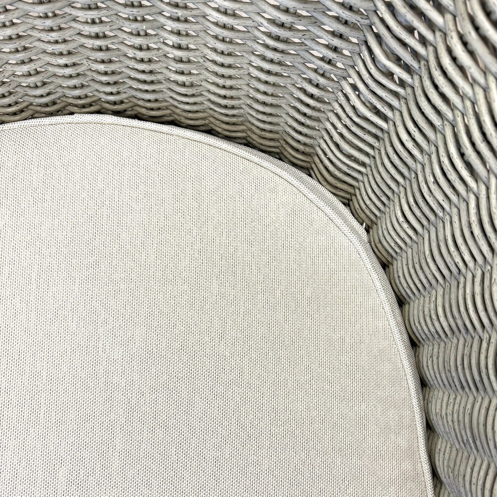 Close-up of grey woven rattan wicker chair with beige cushion, showcasing texture and craftsmanship for outdoor furniture.