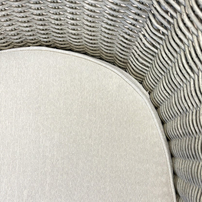 Close-up of grey woven rattan wicker chair with beige cushion, showcasing texture and craftsmanship for outdoor furniture.